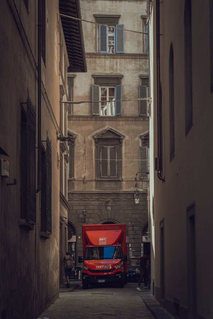 A red truck maneuvers through a narrow alley in historic Florence, Italy.