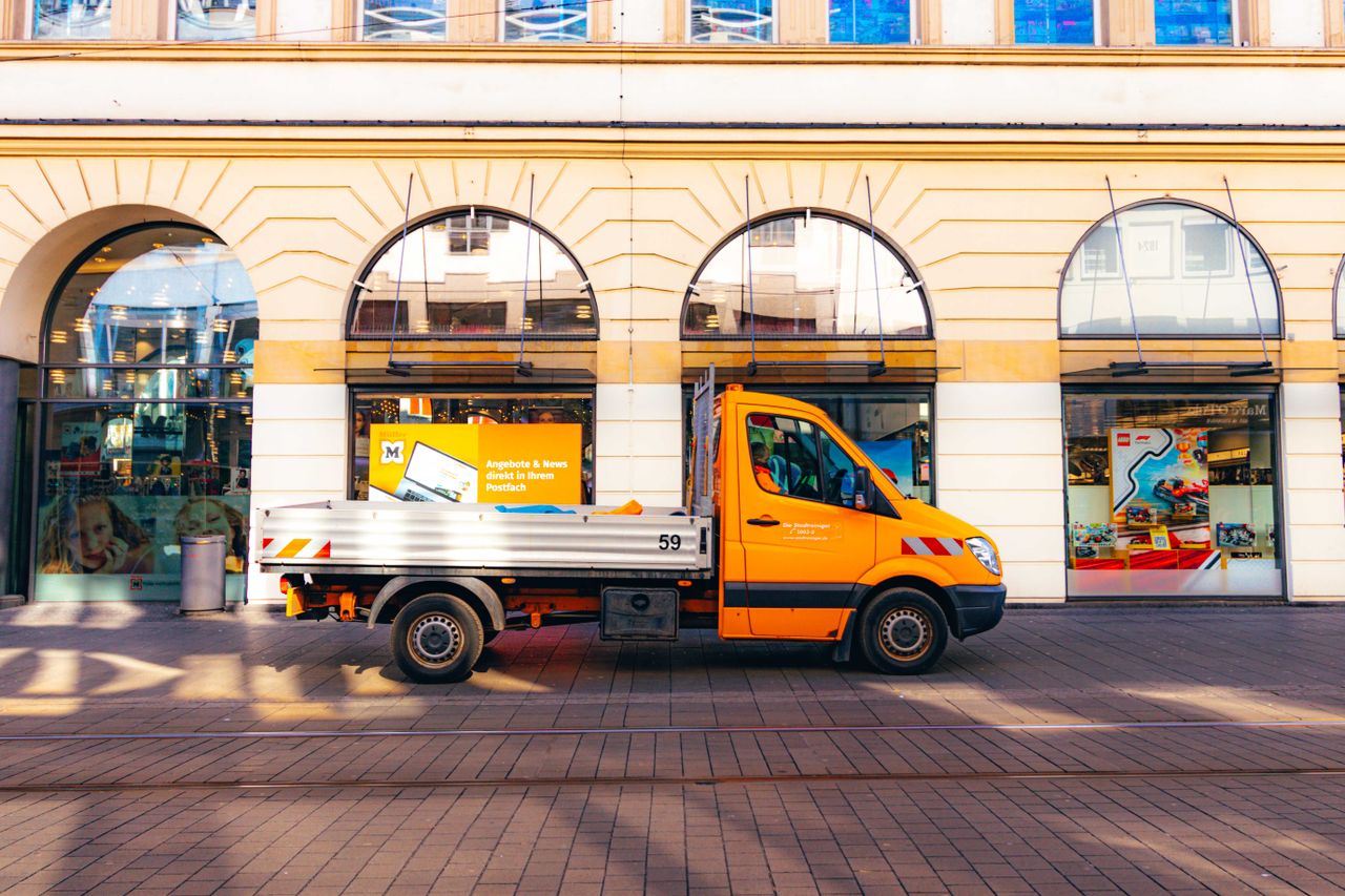 A vibrant orange truck parked against classic European architecture in Kassel, Germany.